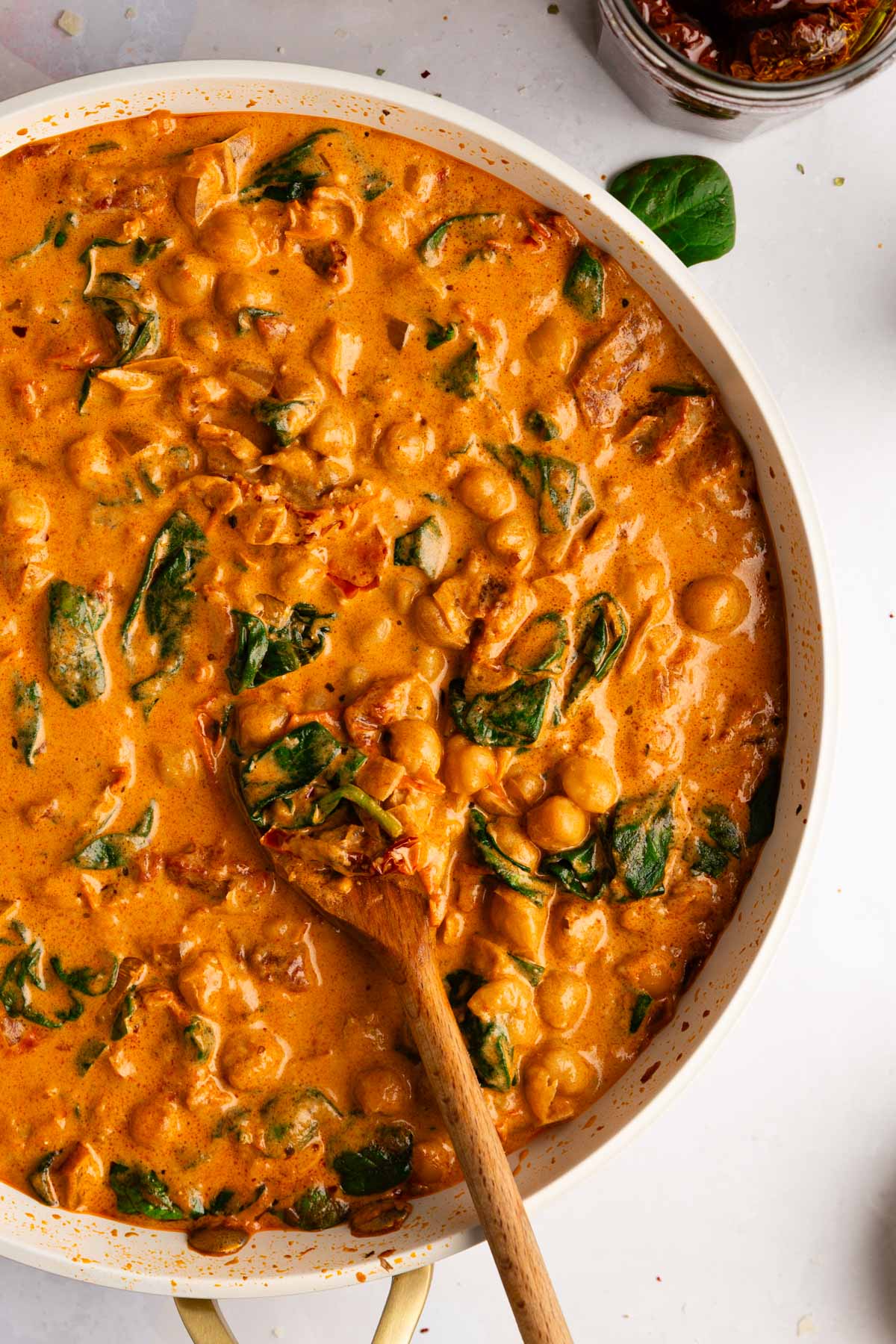 A closeup overhead photo of a skillet filled with creamy Tuscan chickpeas, also known as Marry Me Chickpeas, in a creamy sauce with sun-dried tomatoes, fresh wilted spinach and served with crusty bread.