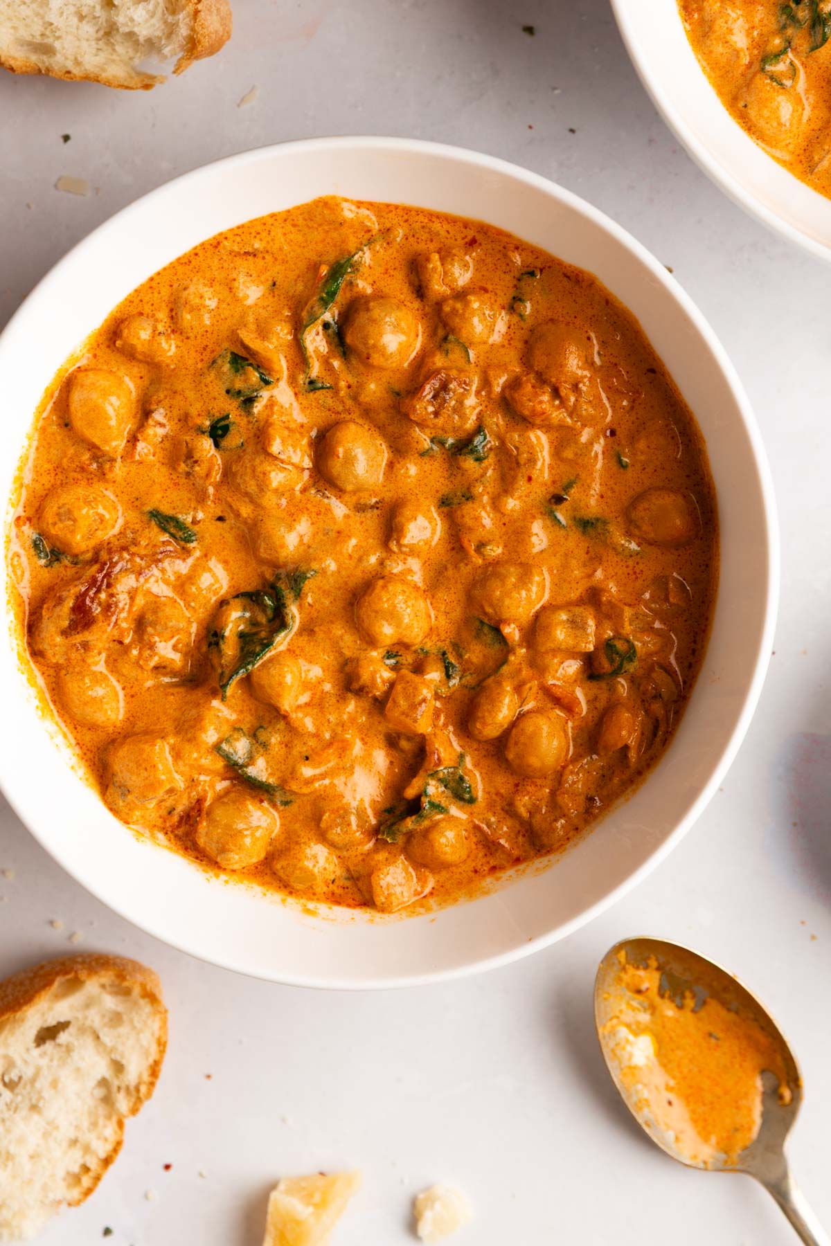 An overhead photo of a bowl of creamy Marry Me Chickpeas served with warm crusty bread on a light gray background.