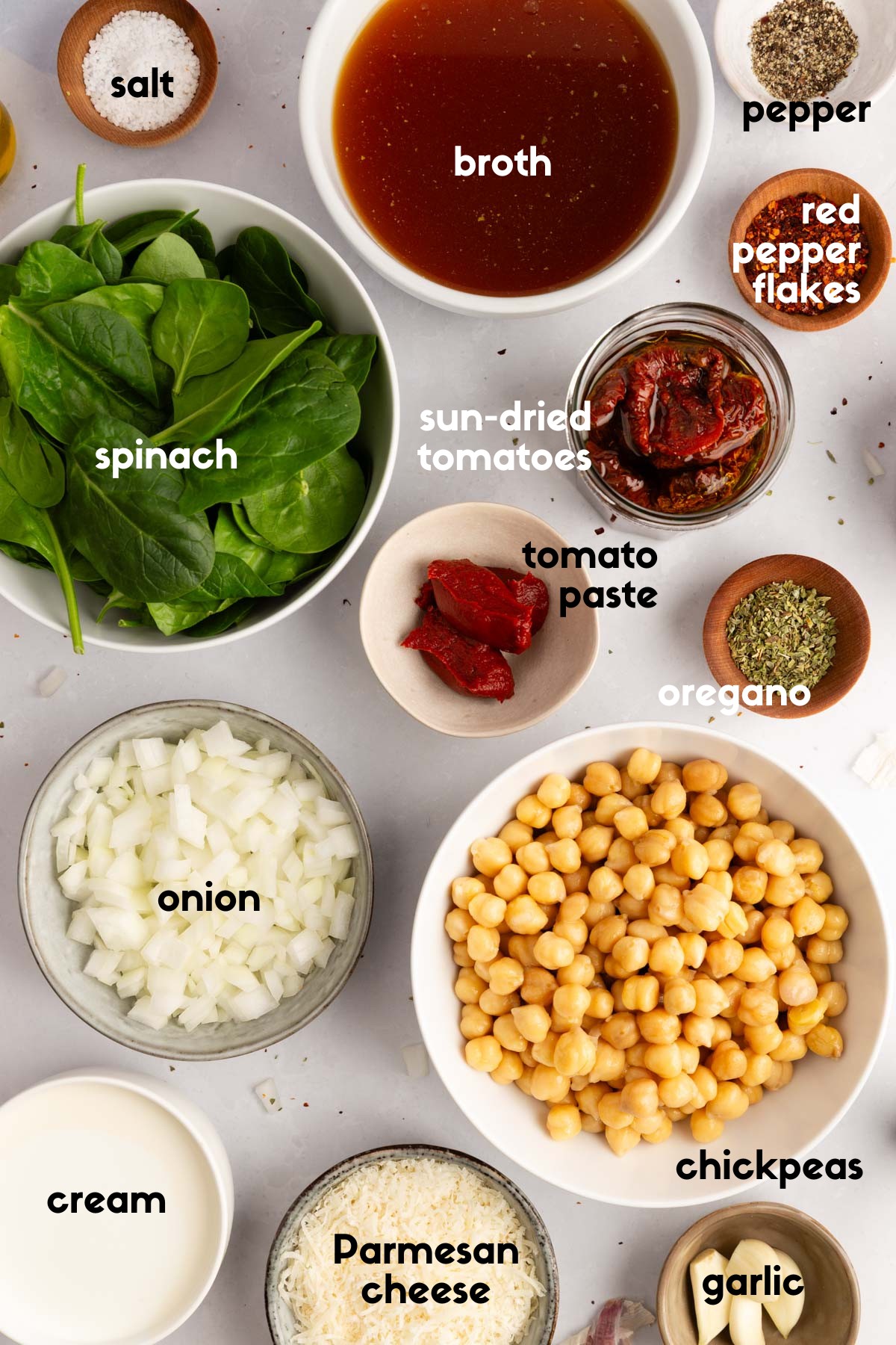 Overhead shot of ingredients for Tuscan Chickpeas, including sun-dried tomatoes, chickpeas, onion, spinach, Parmesan, broth, tomato paste, cream, garlic, and seasonings