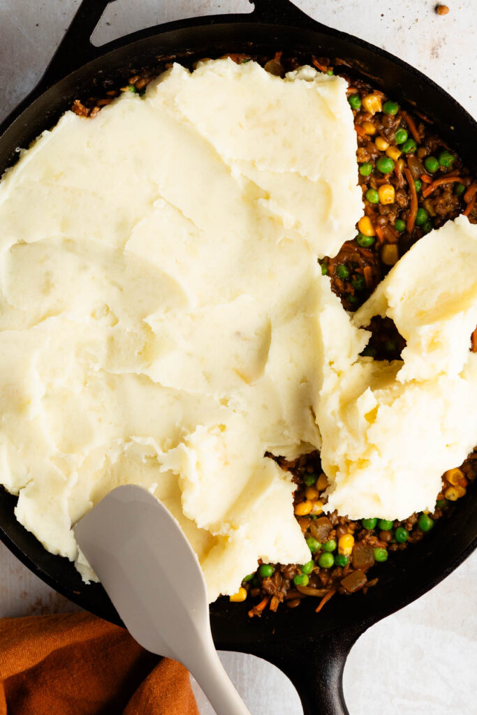 topping the cooked beef with mashed potatoes