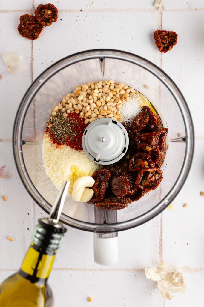 adding all the ingredients needed to make this sun-dried tomato pesto into the food processor