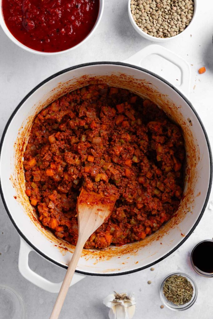 Stirring in tomatoes, water, lentils, soy sauce, and seasoning