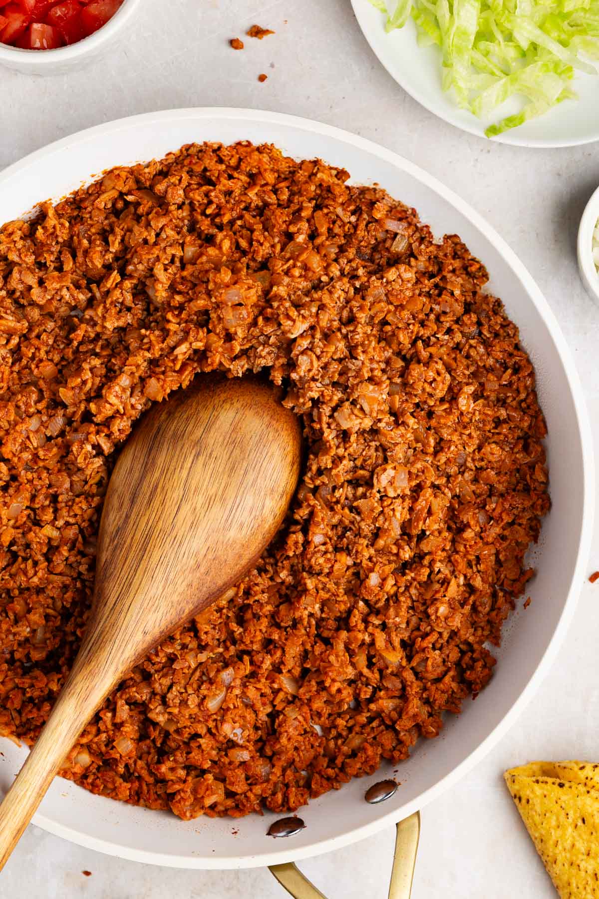 closeup overhead of textured vegetable protein taco meat in a white skillet with a wooden spoon