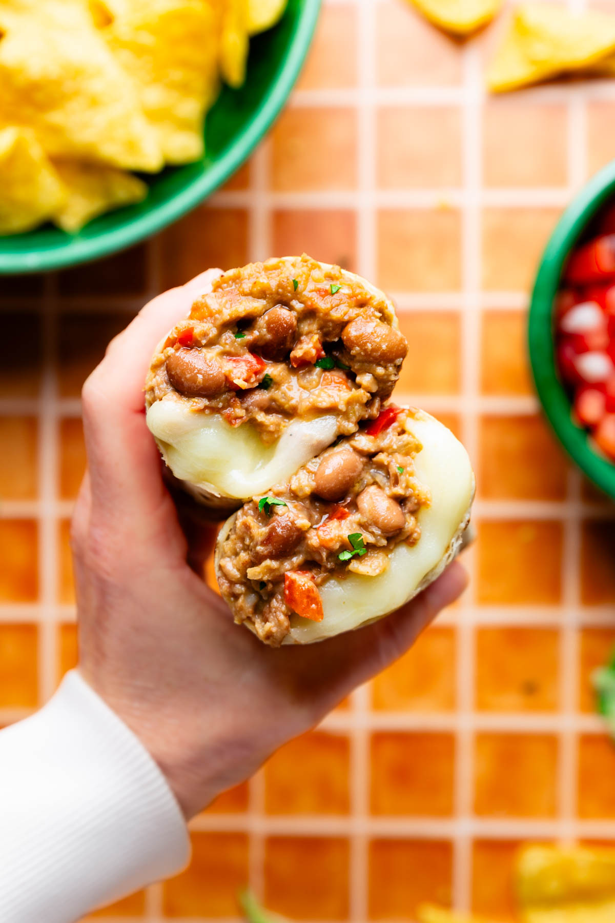 Cheesy Pinto Bean Burritos cut in half with a hand holding it to show the filling