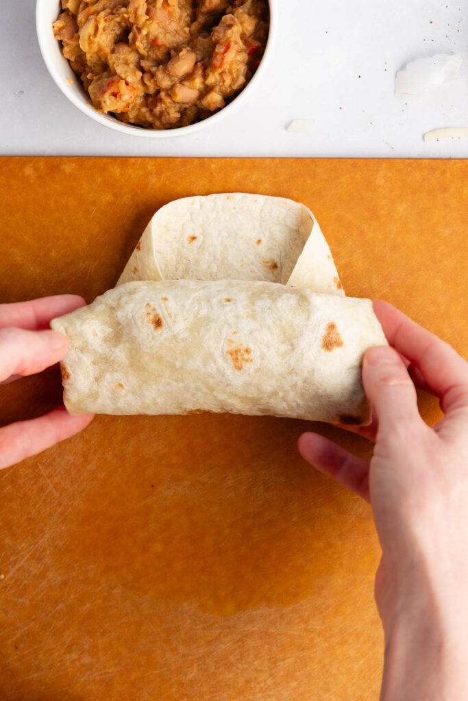 rolling the flour tortilla once it is full of ingredients