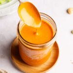 Spoon dipping into a jar of dairy free buffalo sauce.