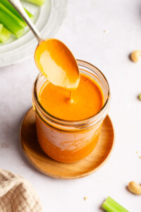Spoon dipping into a jar of dairy free buffalo sauce.