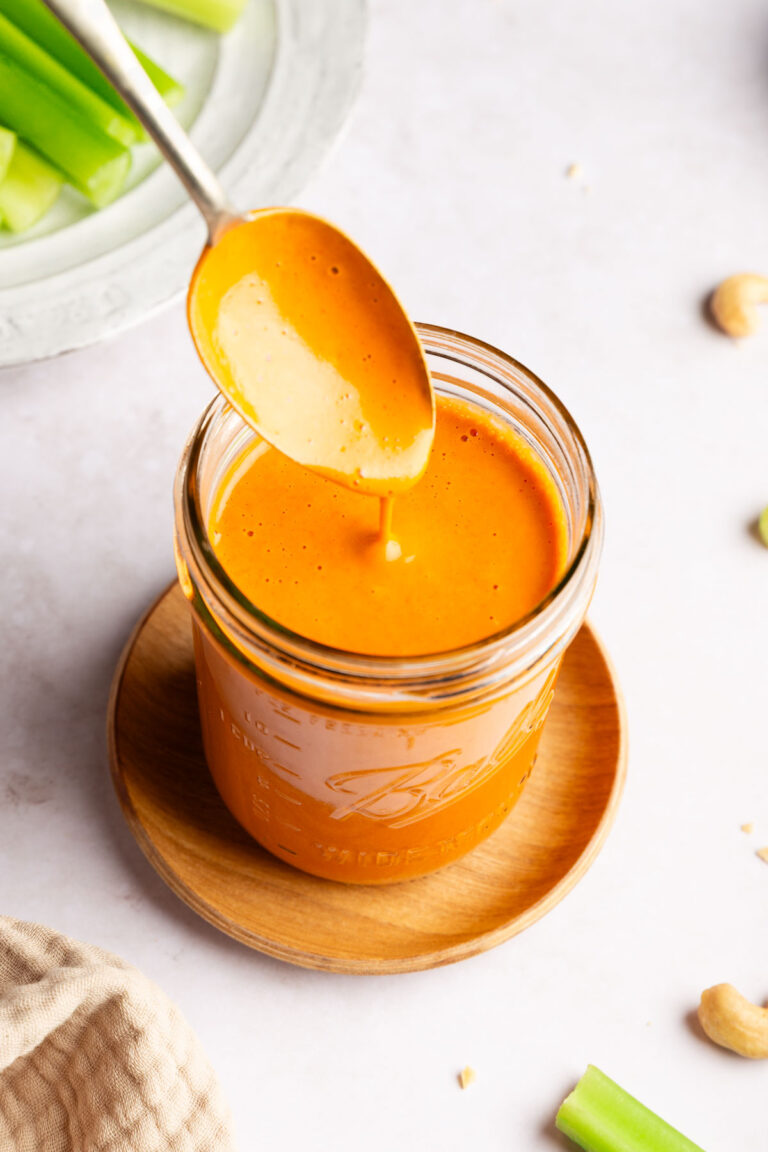 Spoon dipping into a jar of dairy free buffalo sauce.
