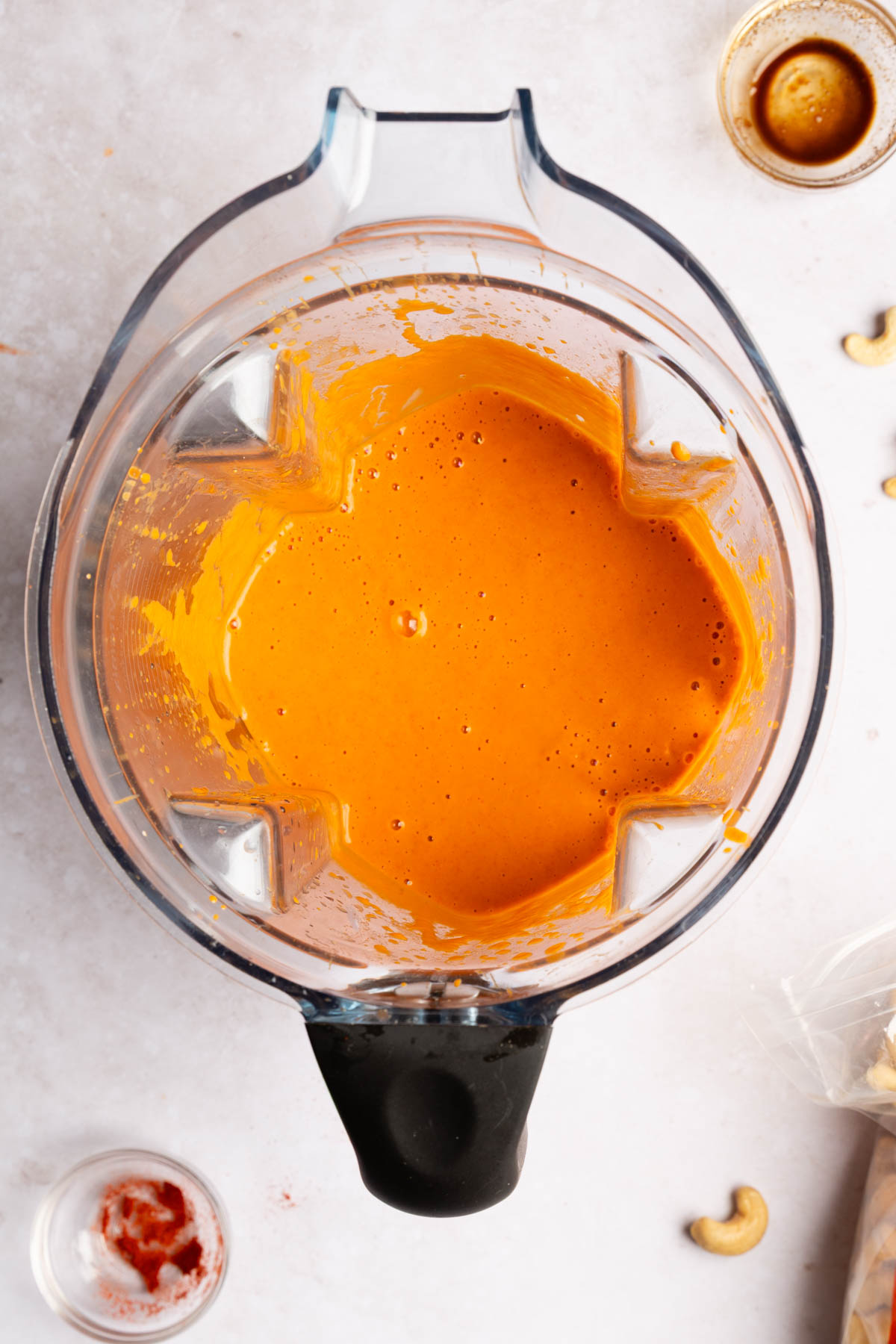 Top down photo of smooth, homemade vegan buffalo sauce in a blender on a white stone background