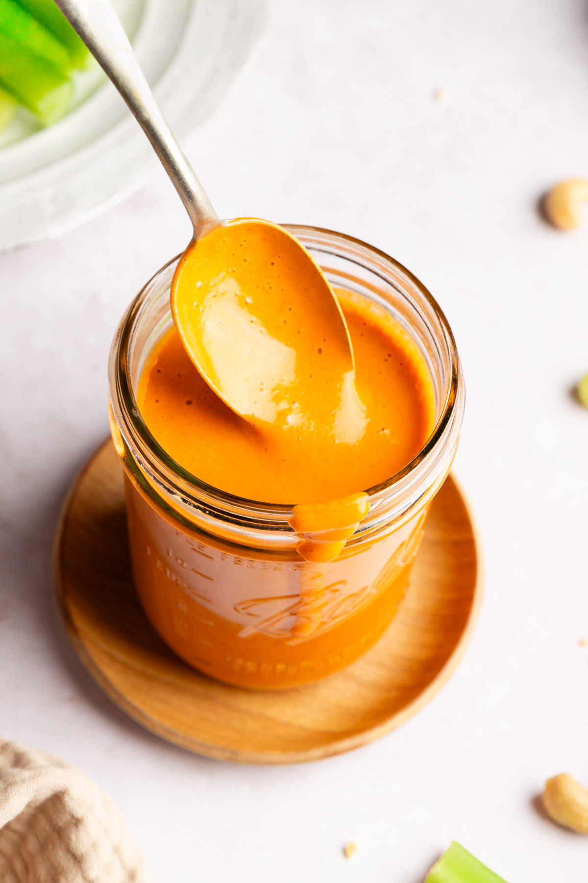 Closeup photo of a spoon dipping into a jar of dairy free vegan buffalo sauce.