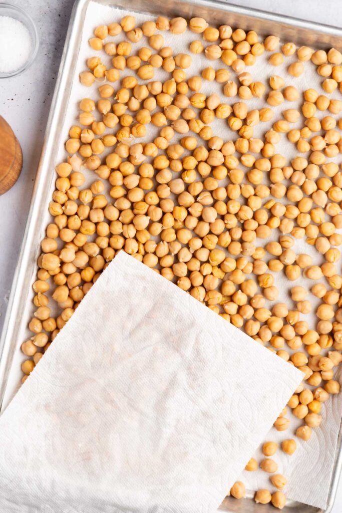 Rinsed chickpeas on a baking sheet being patted dry. 