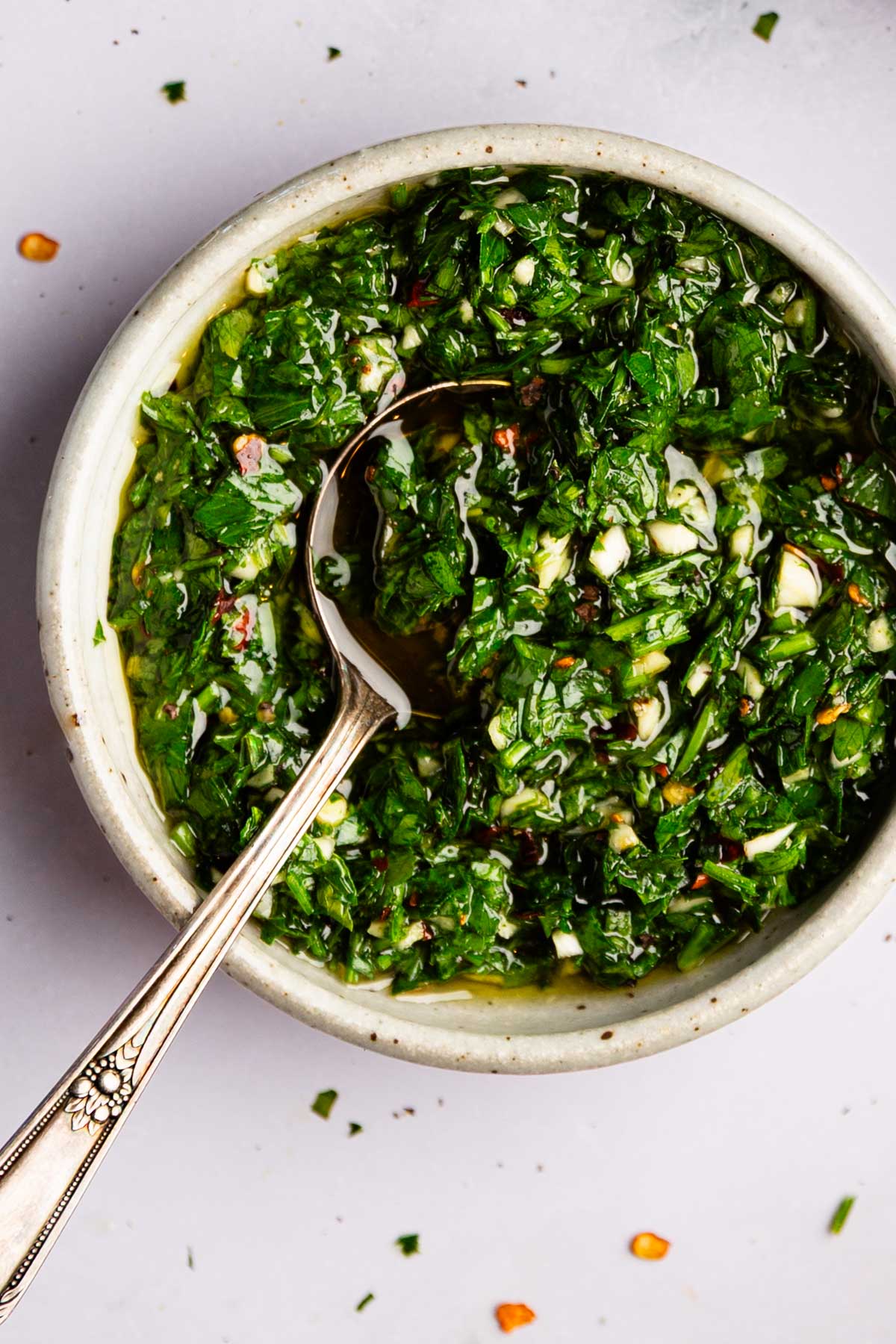 White bowl full of garlic parsley sauce with a spoon in it.