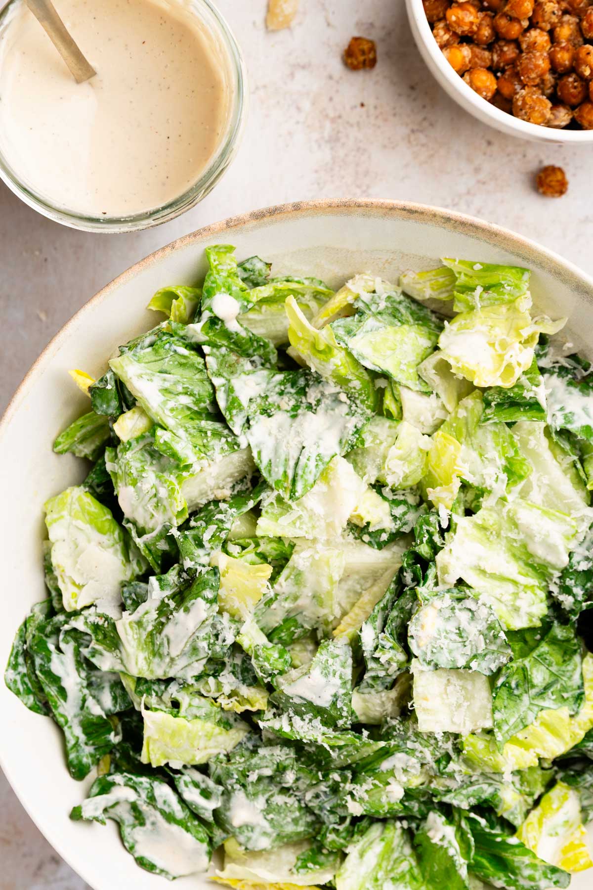 overhead photo of a healthy caesar salad dressing in a glass jar next to a bowl of dressed romaine lettuce and crispy parmesan chickpeas