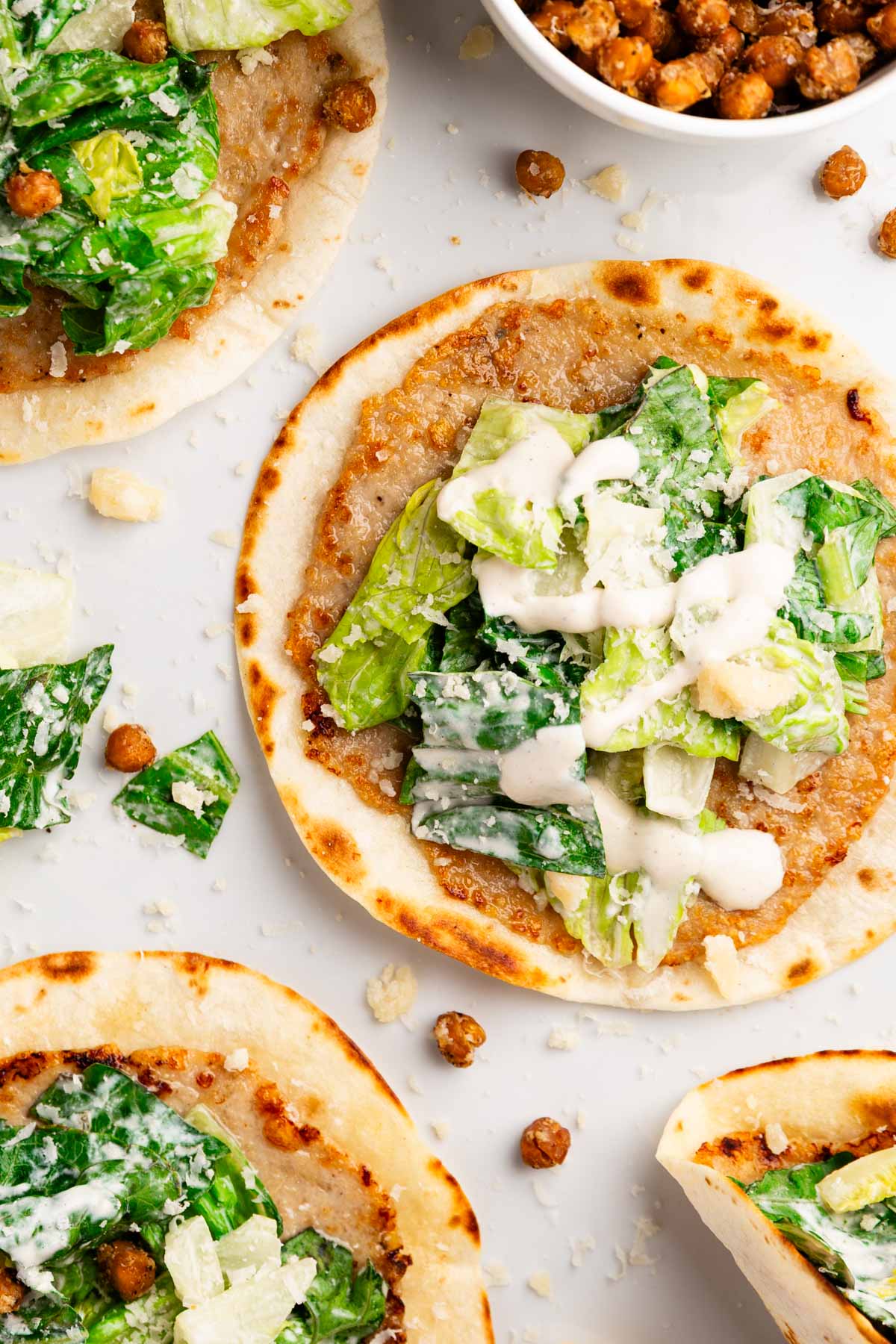 overhead photo of smashed chicken tacos topped with caesar salad and crispy chickpeas, parmesan and caesar dressing on a light background