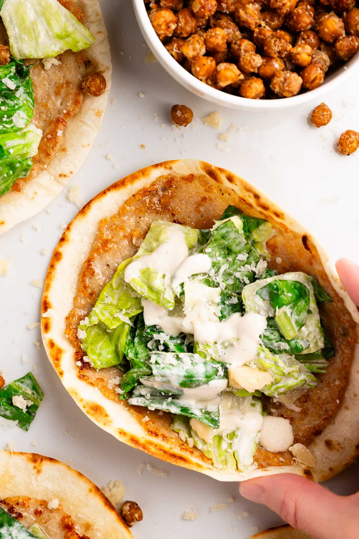 overhead closeup photo of a hand picking up and folding a smashed chicken caesar taco