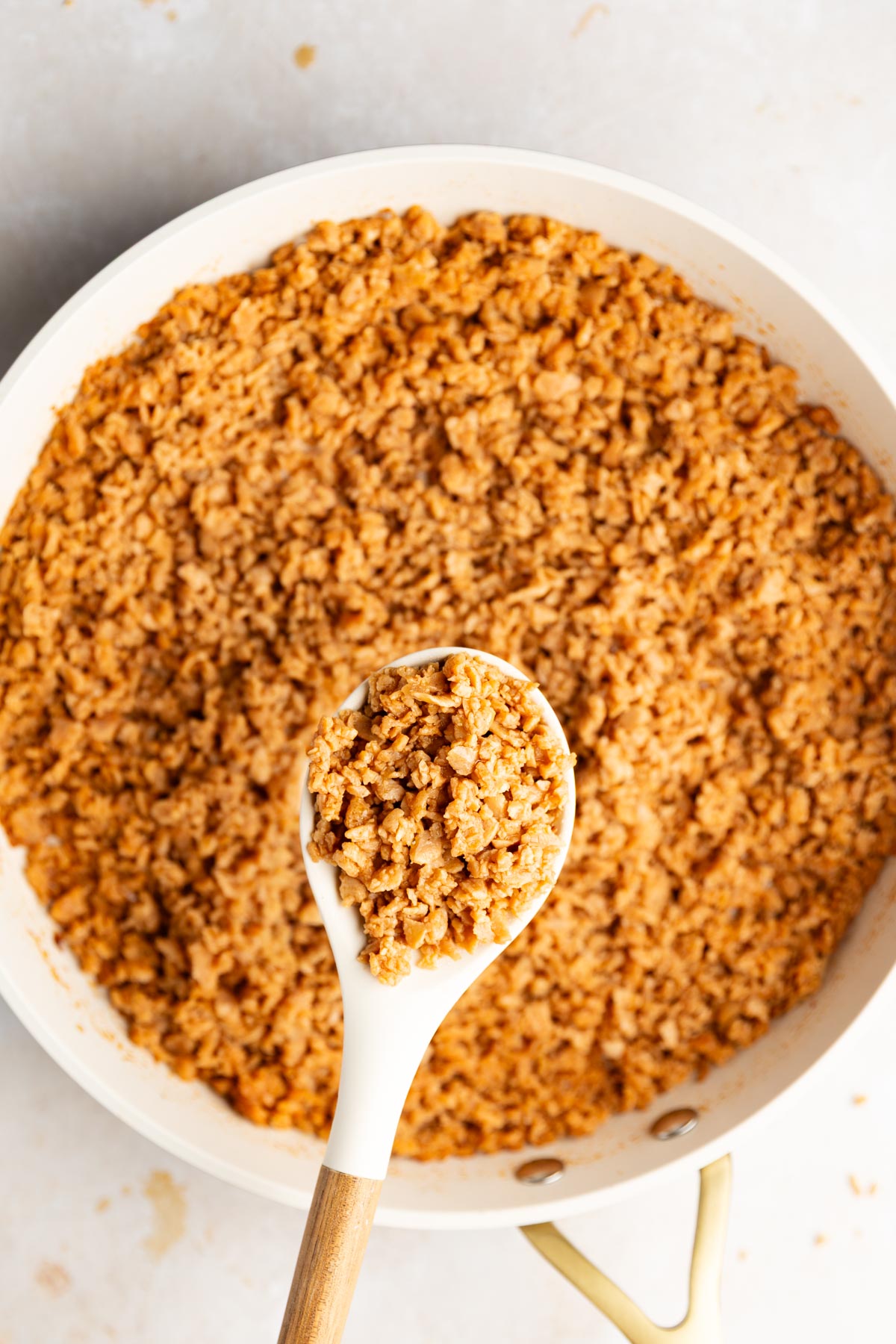 Cooked, seasoned TVP in a white skillet with a white spoon lifting a scoop.