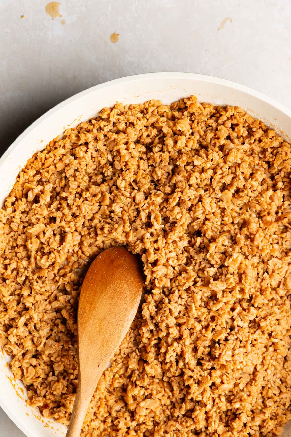 overhead photo of a white skillet with cooked tvp (textured vegetable protein) and a wooden spoon on a light stone background