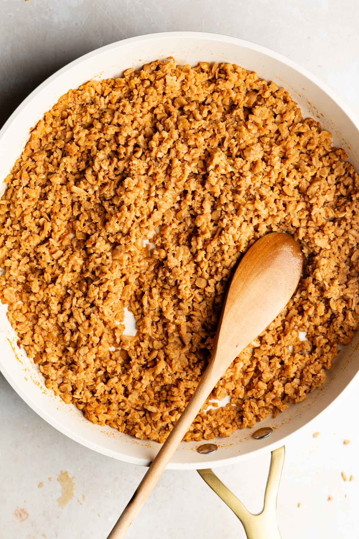 Seasoned vegan ground beef made with TVP in a white skillet, with a wooden spoon resting in the crumbles.