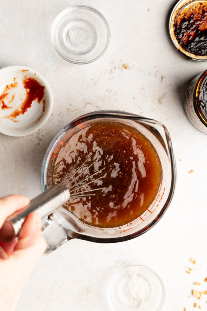 Whisking vegan beef broth, tomato paste and spices together in a glass measuring cup.