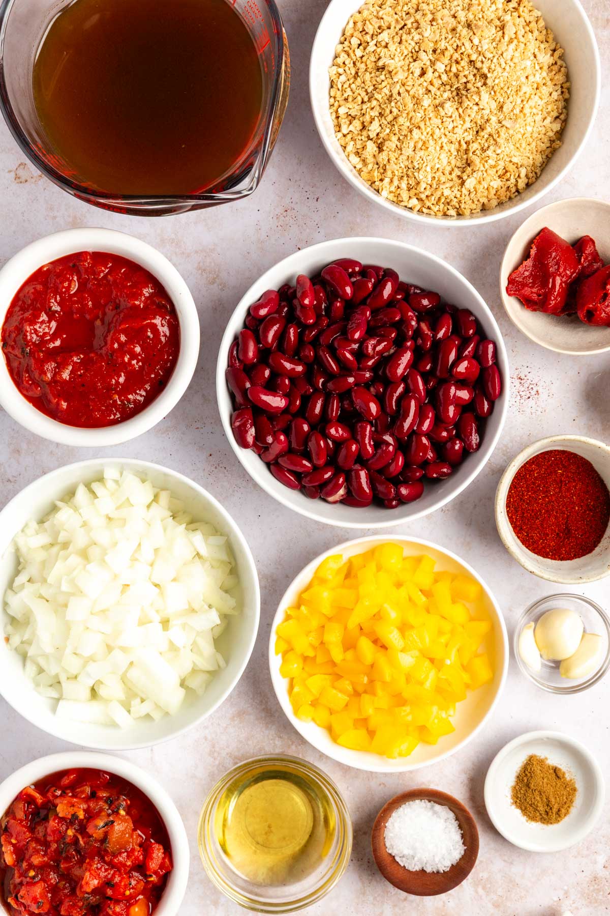 Ingredients used for tvp chili including broth, tvp, beans, crushed and diced tomatoes, onion, bell pepper, garlic, avocado oil, salt, cumin, chili powder, and tomato paste