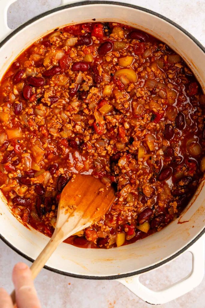Overhead photo of vegan tvp chili simmering and being stirred in a white pot