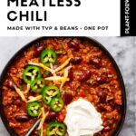 Bowl of hearty meatless chili with kidney beans, jalapeño slices, shredded cheese and sour cream on a marble surface. White text panel above reads Healthy Vegetarian Dinner, Hearty Meatless Chili, made with TVP and beans, one pot. A Get the Recipe button sits in the corner.
